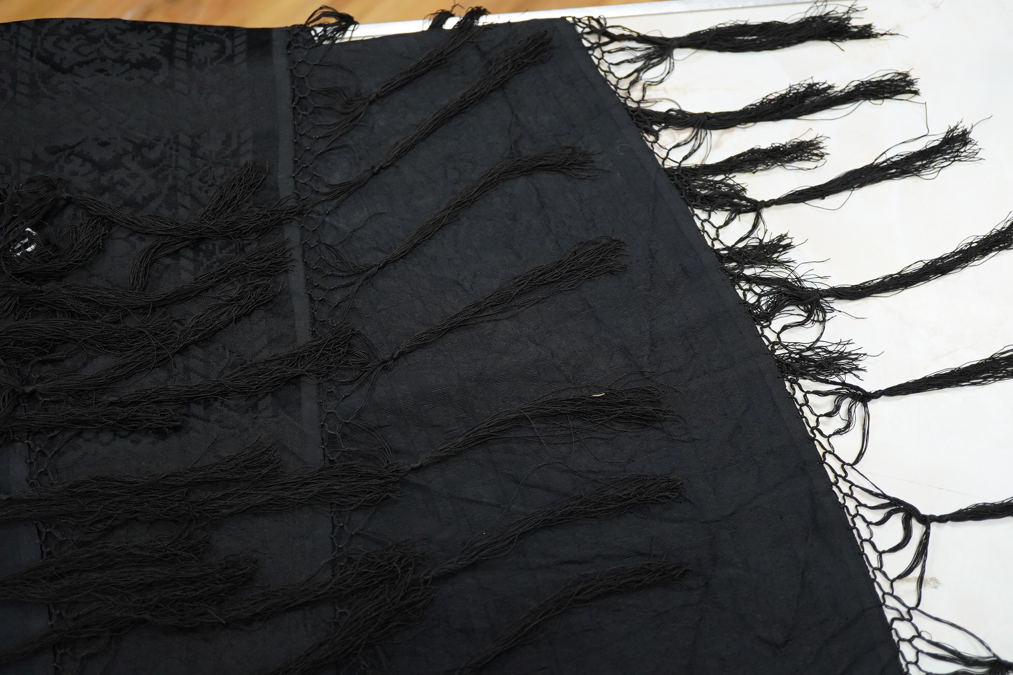 A Edwardian black silk damask paisley patterned shawl. Possibly a mourning shawl.178cm x 156cm. Condition - one small hole, otherwise good.